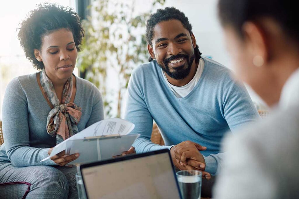 Two adults sit together reviewing insurance documents and discussing options at a kitchen table.