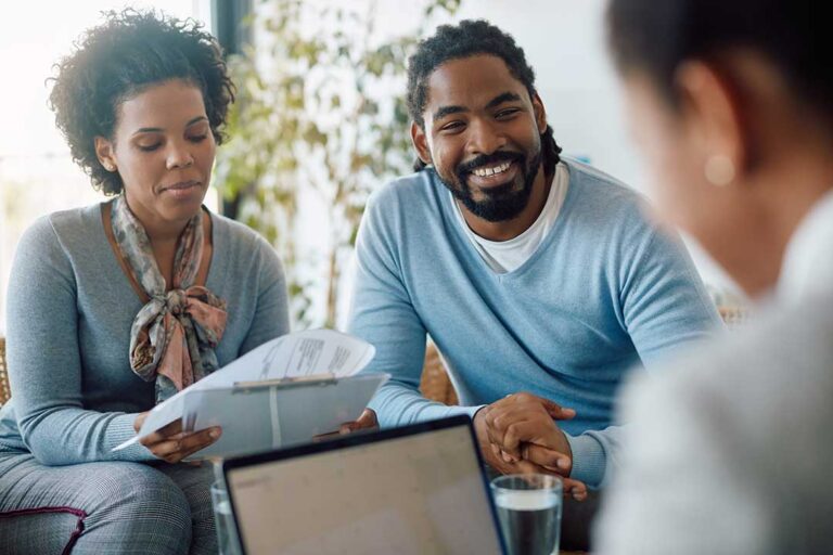 Two adults sit together reviewing insurance documents and discussing options at a kitchen table.