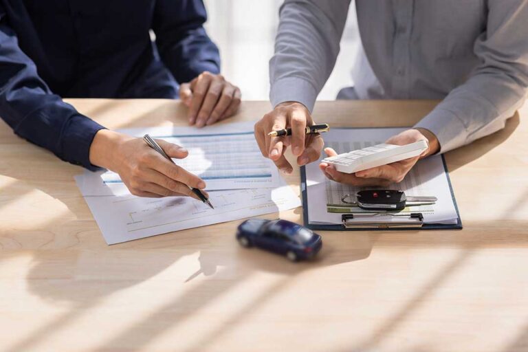 Adults review life insurance paperwork beside a calculator and family budget documents at a kitchen table.